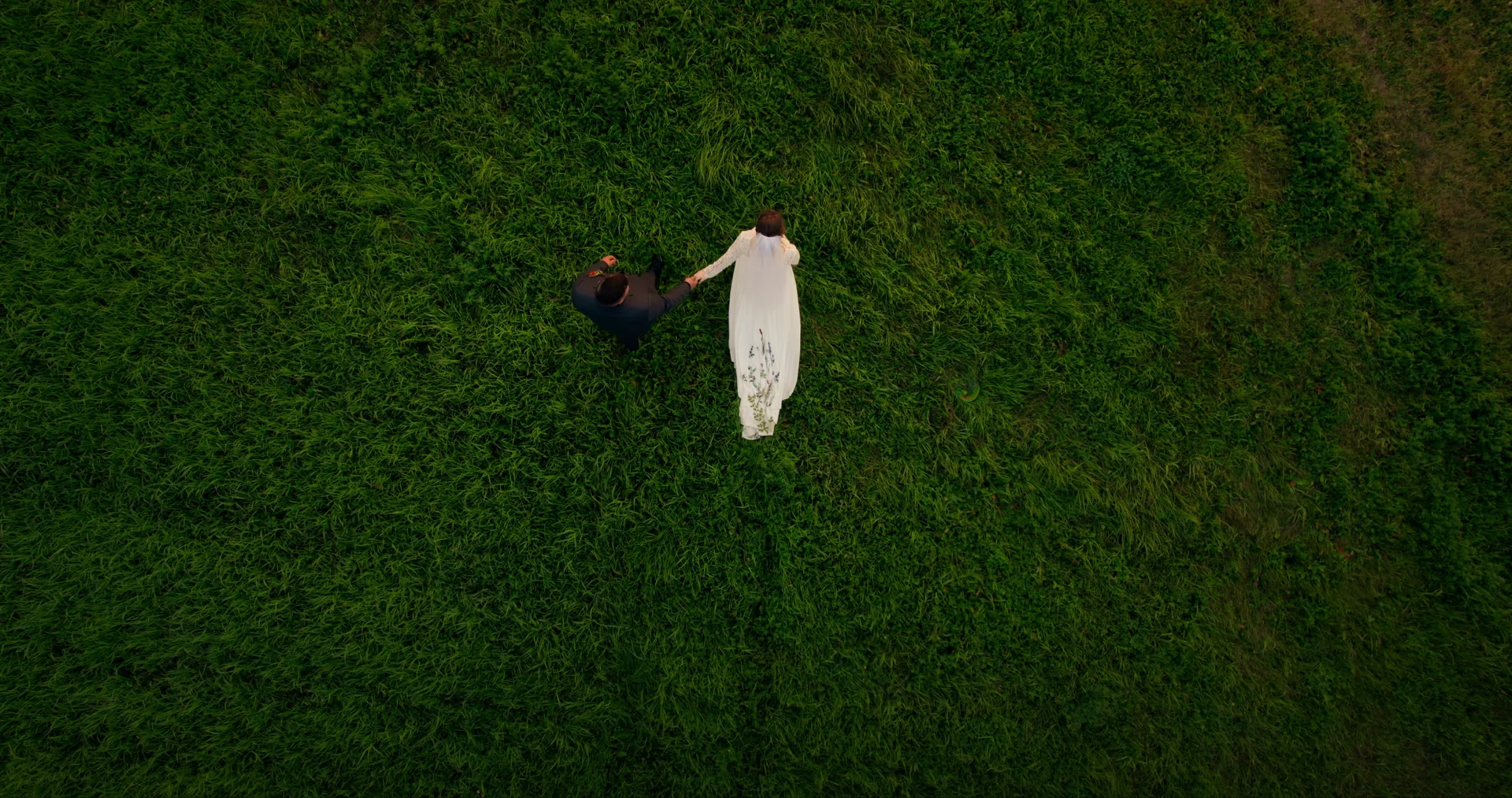 An aerial view of newlyweds holding hands in a green meadow